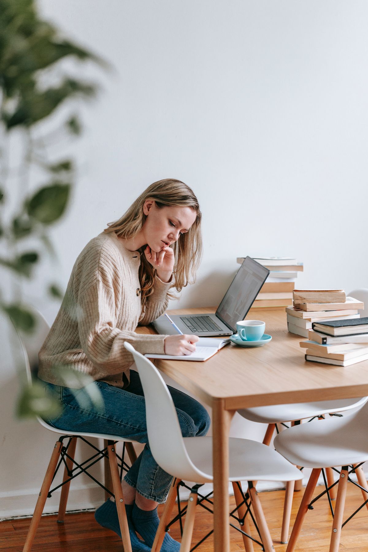 Une femme prend des notes à côté de livres et d’un ordinateur — photographie d’illustration
